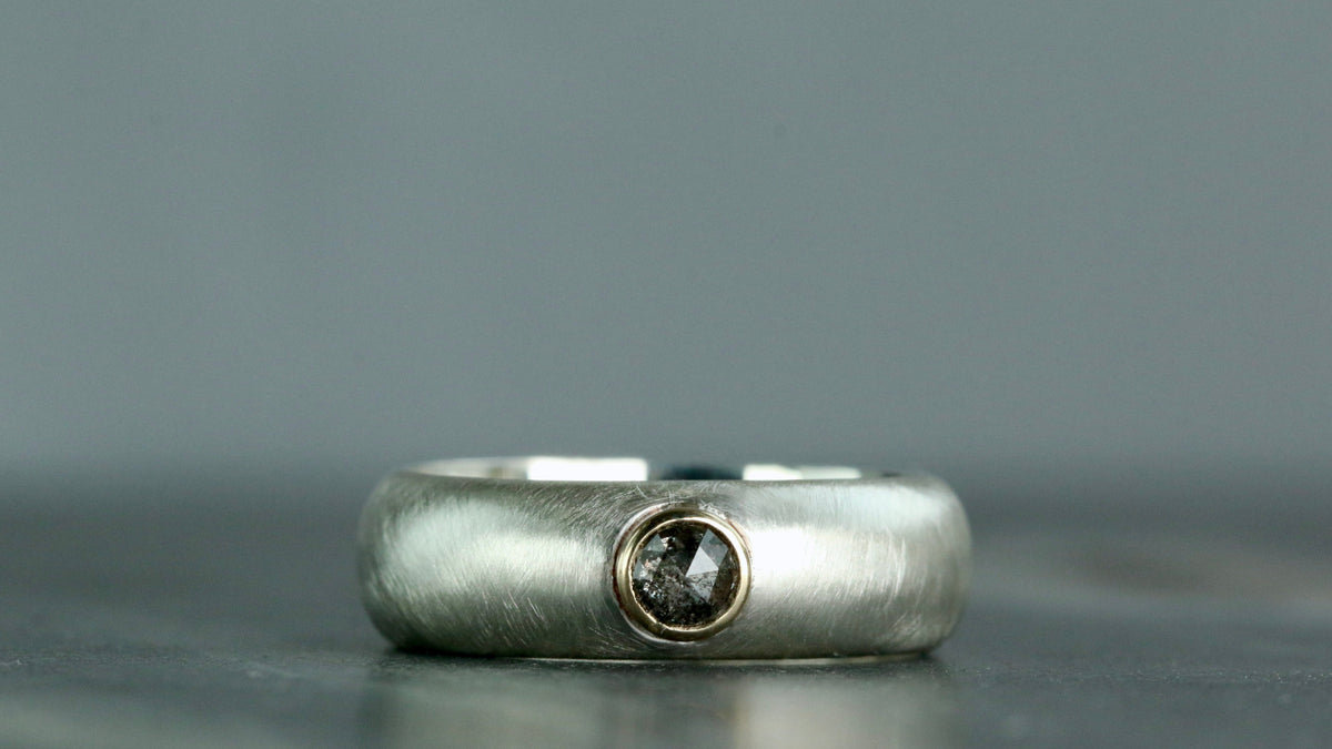 A textured sterling silver band ring with a small bezel-set, round, salt and pepper rose cut cabochon in the centre of a raised gold bezel.